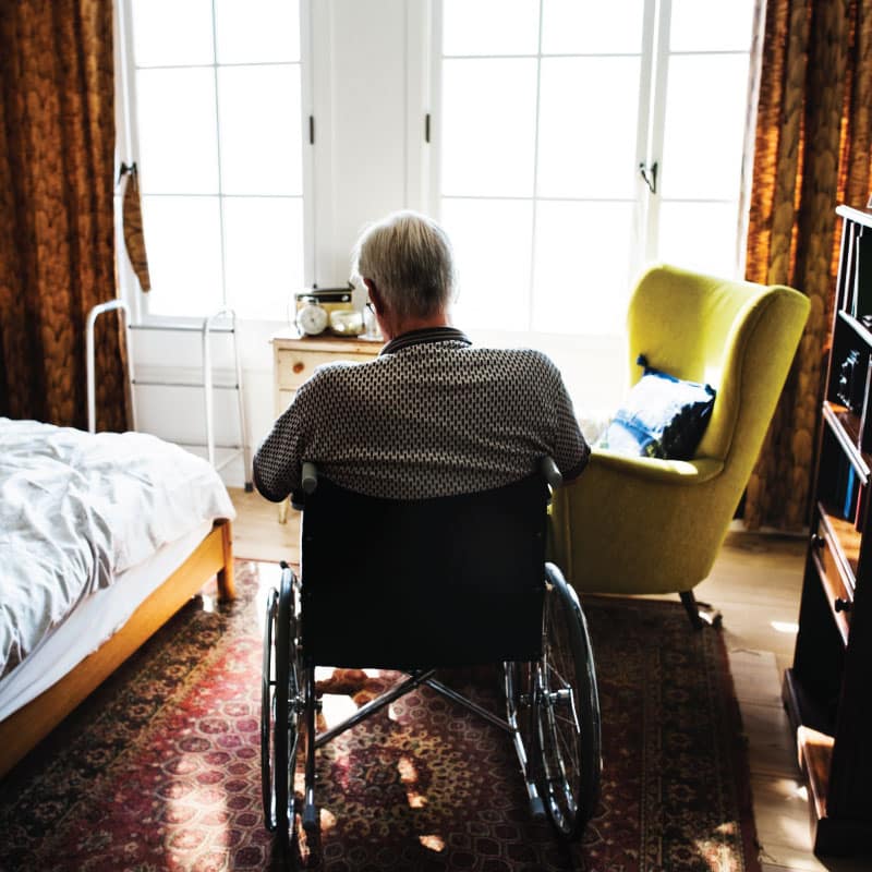 an elderly man looks out the window in a nursing home facility