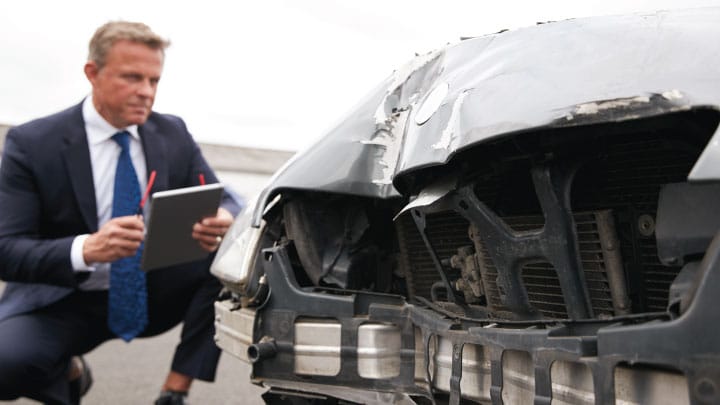 an insurance adjuster views damage of a car that was involved in an auto accident