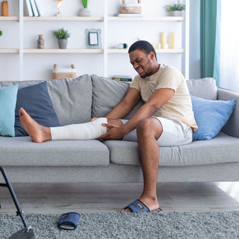 Man who has suffered a serious injury to his leg positions it on a couch uncomfortably